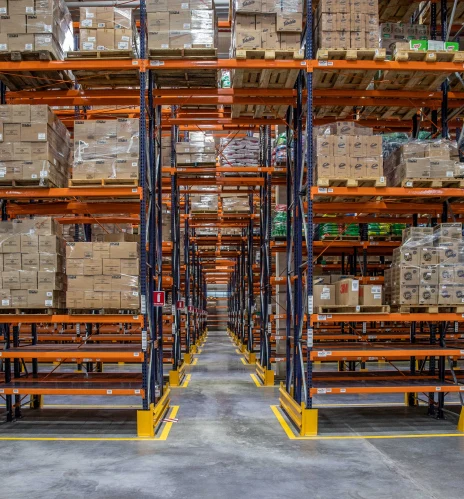 Almacén industrial con estanterías naranjas llenas de cajas y productos, logística y distribución eficiente con Dinpro.